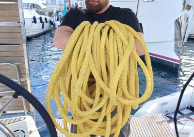 Załogant gotów do zawiezienia liny cumowniczej na brzeg. Jak widać stoimy przed dziobami jachtów zacumowanych do nabrzeża. Tak właśnie cumuje się na Hydrze.